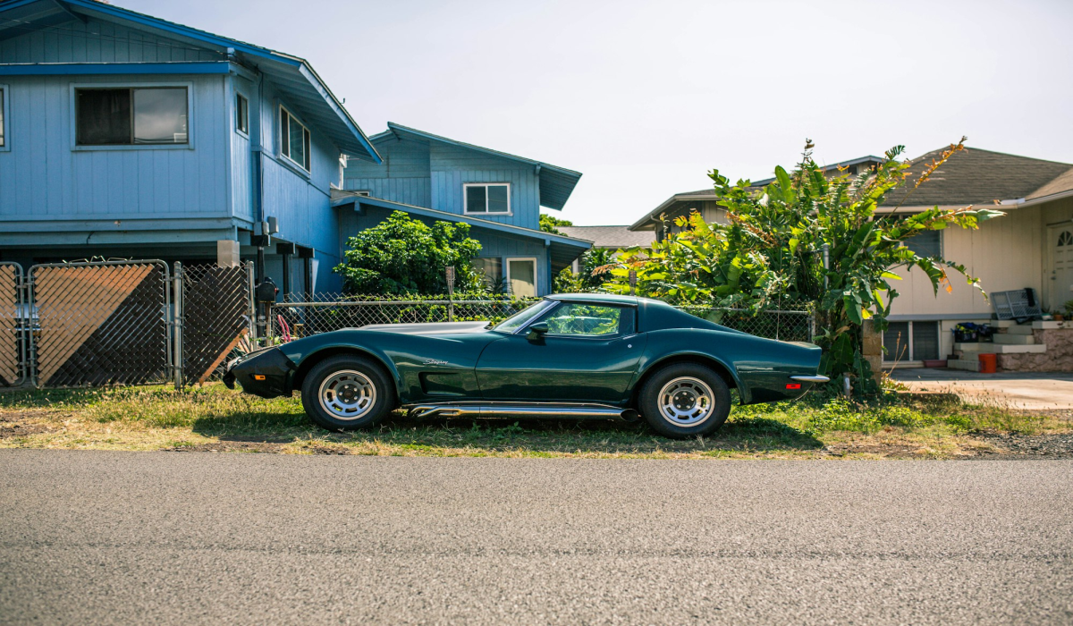 Classic Green Sports Car Parked By Blue Residential House Amidst Suburban Greenery